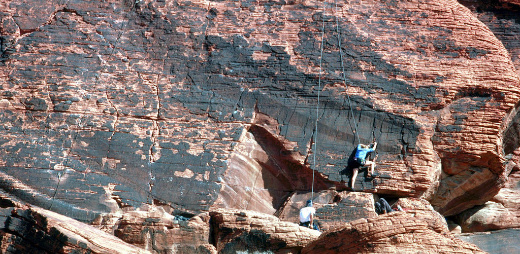 people scaling vertical wall of rock