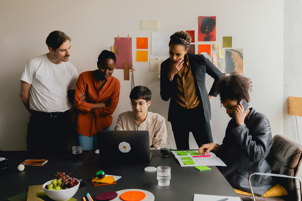 people in office gathered around computer and on phone